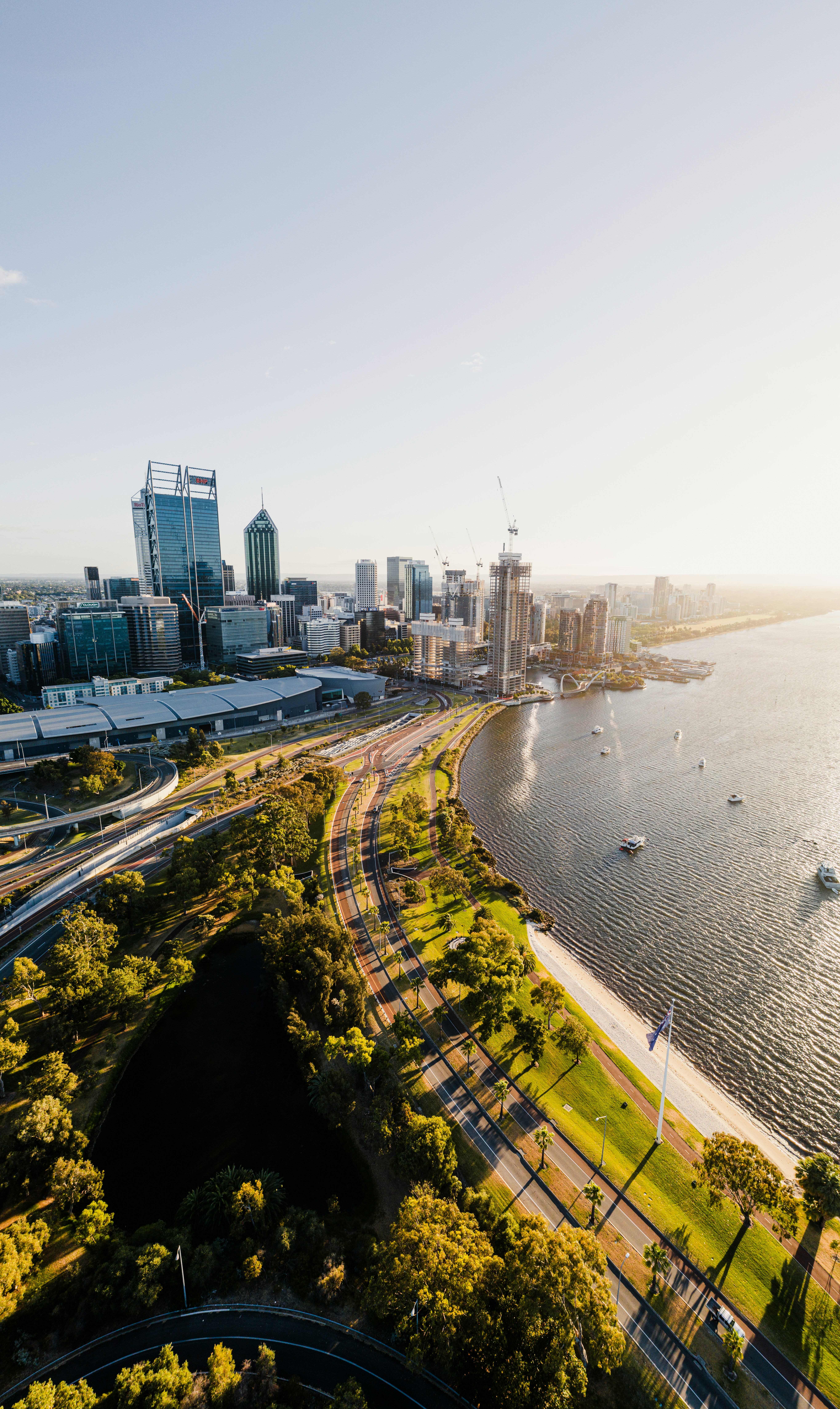 WA Gov: Aerial view of Perth, Western Australia, showing the Swan River, city skyline, green spaces, and infrastructure on a sunny day.